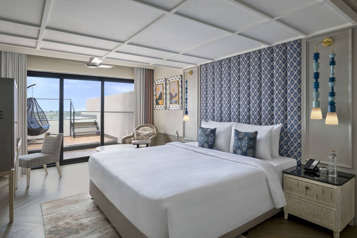 A hotel room with a large bed, a chair, a nightstand, and a view of the outdoors.