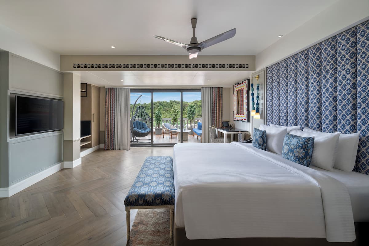 A spacious hotel room with a large bed, a flat-screen TV, a ceiling fan, and a balcony with a view of the outdoors.