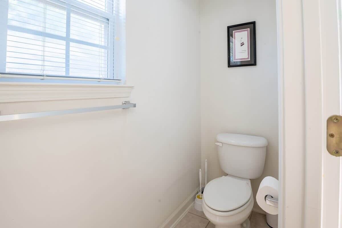 Et lille, rent badeværelse med toilet, et billede i ramme på væggen og et vindue med skodder.