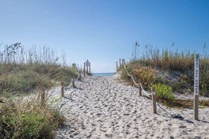 Un sentier de plage sablonneux, bordé de poteaux en bois et de cordes qui indiquent le chemin.