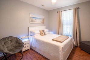 Un dormitorio con cama, una silla, una mesita de noche y un cuadro en la pared.