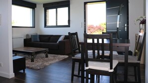 A modern living room with a dark wood dining table, a black sofa, and a large window with a view of pink flowers. - 2 pieces, garden level, Vue imprenable sur le Lac Léman (Évian-les-Bains)