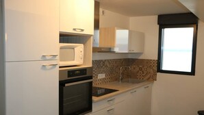 A compact kitchen with white cabinets, a microwave, an oven, and a patterned backsplash. - 2 pieces, garden level, Vue imprenable sur le Lac Léman (Évian-les-Bains)