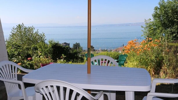 A patio with a table and chairs, overlooking a body of water and greenery. - 2 pieces, garden level, Vue imprenable sur le Lac Léman (Évian-les-Bains)