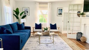 A living room with a blue sofa, white chairs, a coffee table, and a large window. - Maxson House Mystic – Easy Walk to Downtown (Mystic)