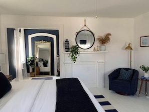 Ein Schlafzimmer mit Bett, Stuhl, Spiegel, Kamin und Pflanze.