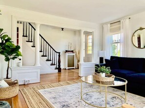 Ein Wohnzimmer mit Treppe, einem dunkelblauen Sofa, einem runden Couchtisch und einem großen Spiegel.