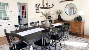 A dining room with a dark wooden table, black chairs, a chandelier, a mirror, and a wooden cabinet. - Maxson House Mystic – Easy Walk to Downtown (Mystic)