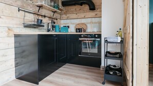 A modern kitchen with wooden walls, black cabinets, and a built-in oven. - Dyffryn Ceri - luxury converted shipping container (Penuwch)