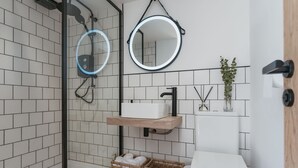 A modern bathroom with white tiled walls, a glass shower enclosure, a wooden vanity, a toilet, and wicker baskets. - Dyffryn Ceri - luxury converted shipping container (Penuwch)