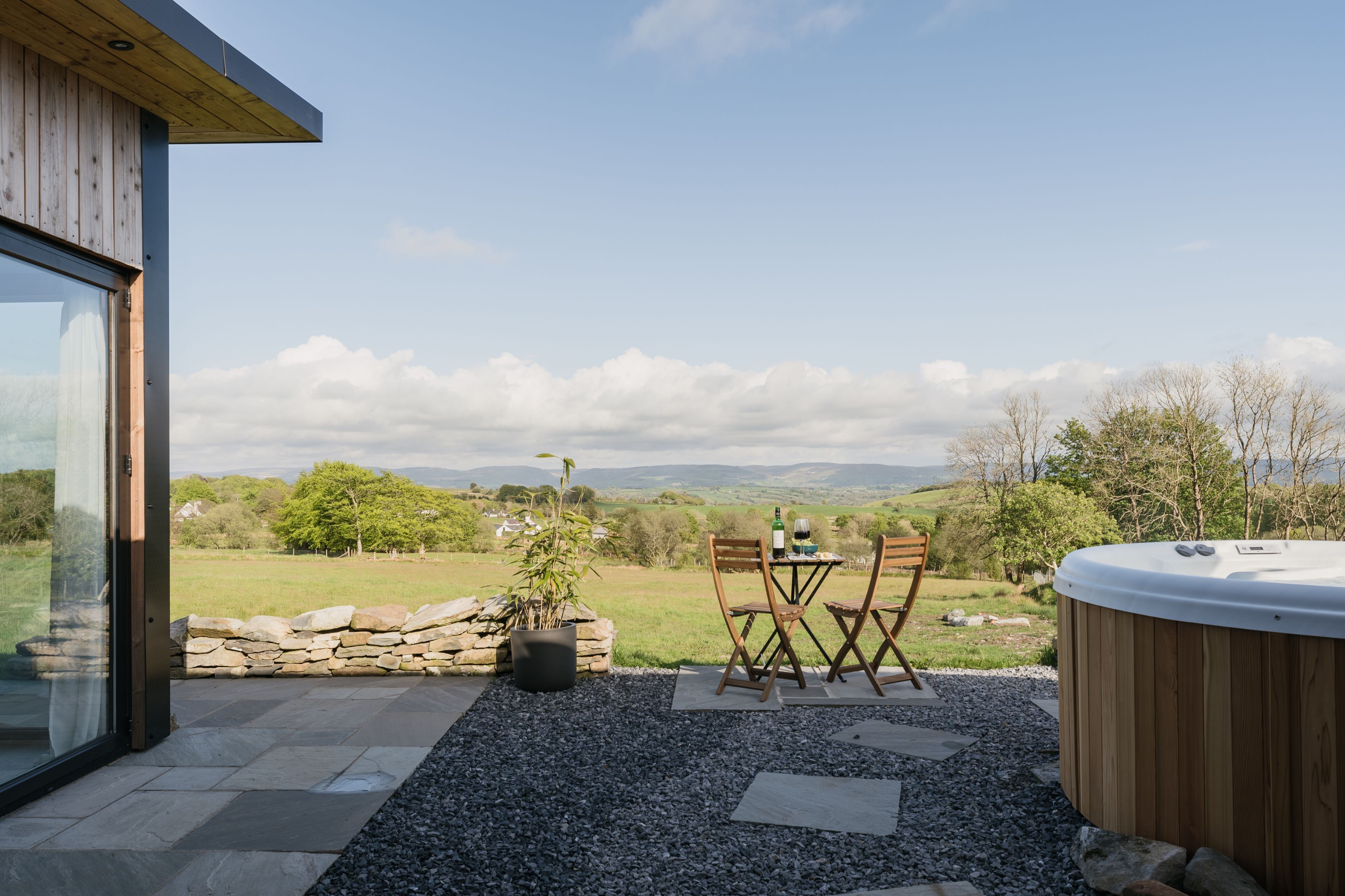 Un patio con hidromasaje, pared de piedra y una mesa con sillas.