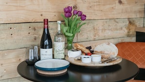 A table with a bottle of wine, a glass, a plate, a vase with flowers, and a bread basket. - Dyffryn Ceri - luxury converted shipping container (Penuwch)