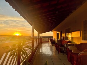 A covered balcony with a view of the sunset, a tiled floor, and a seating area with a sofa and chairs. - Pousada B&B (Capivari)