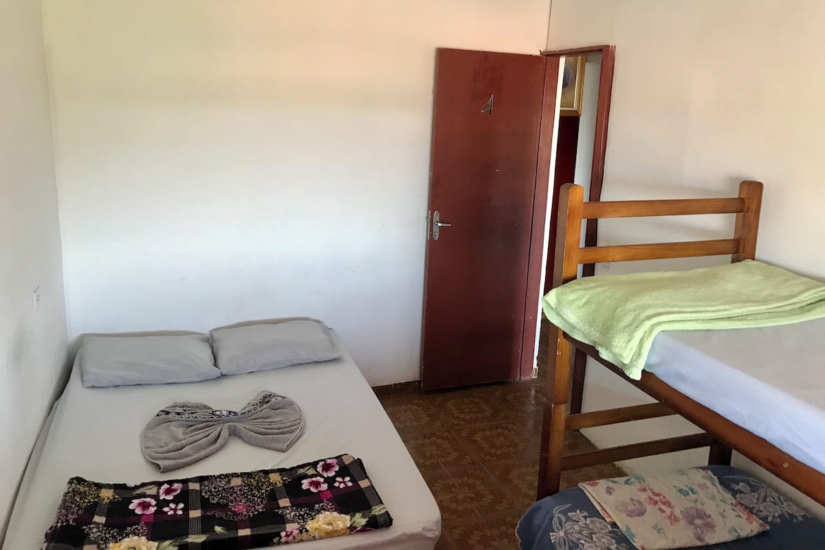 Une petite pièce simple, avec un lit, une chaise en bois et une porte.