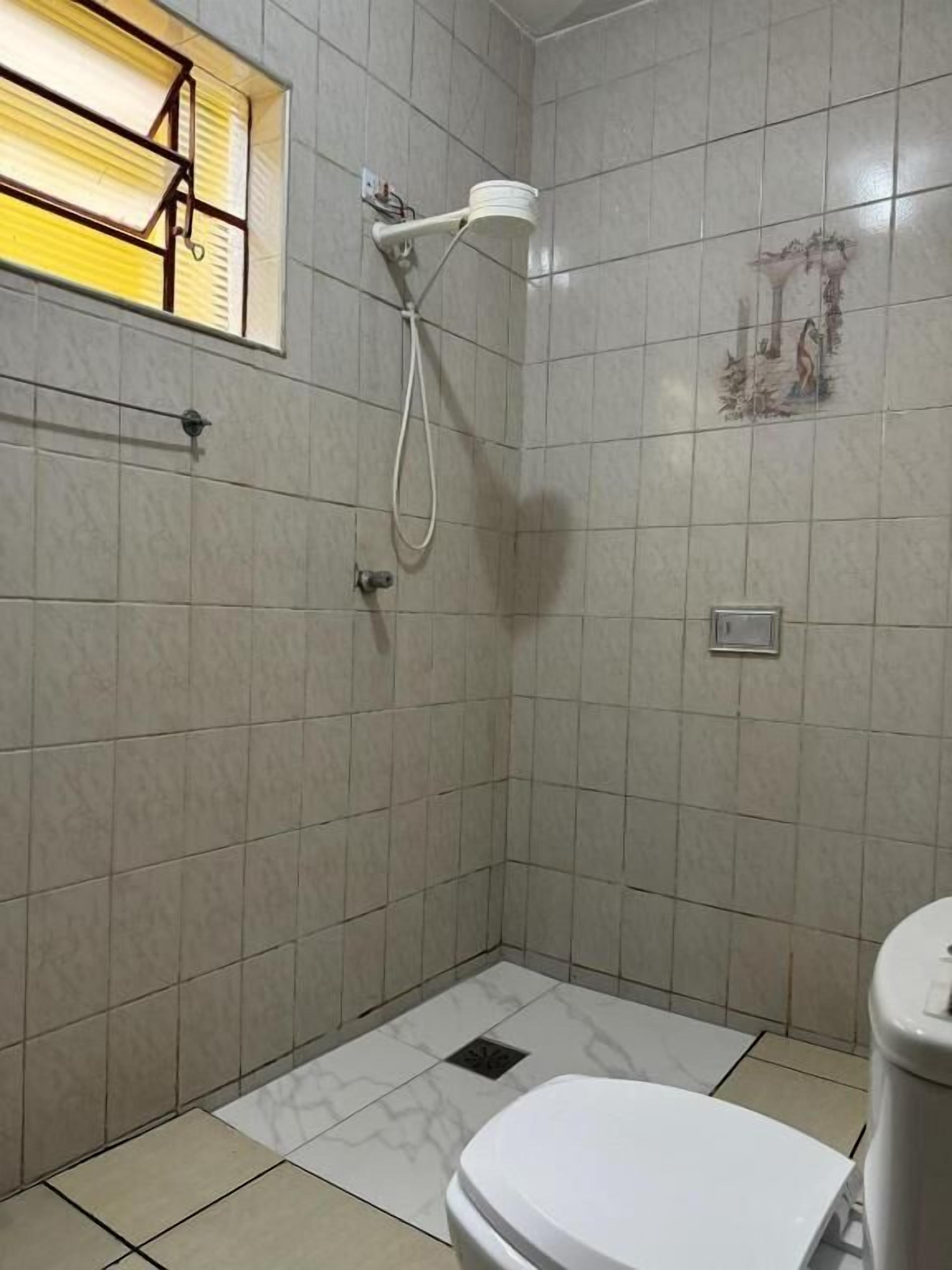 Un baño pequeño con azulejos, que incluye un inodoro, una ducha y una ventana con persianas.