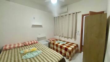 A small, clean room with two beds, a ceiling fan, and a window with curtains.