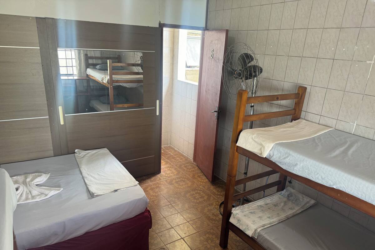 Une chambre de dortoir avec deux lits superposés, une armoire en bois, un ventilateur et un sol carrelé.