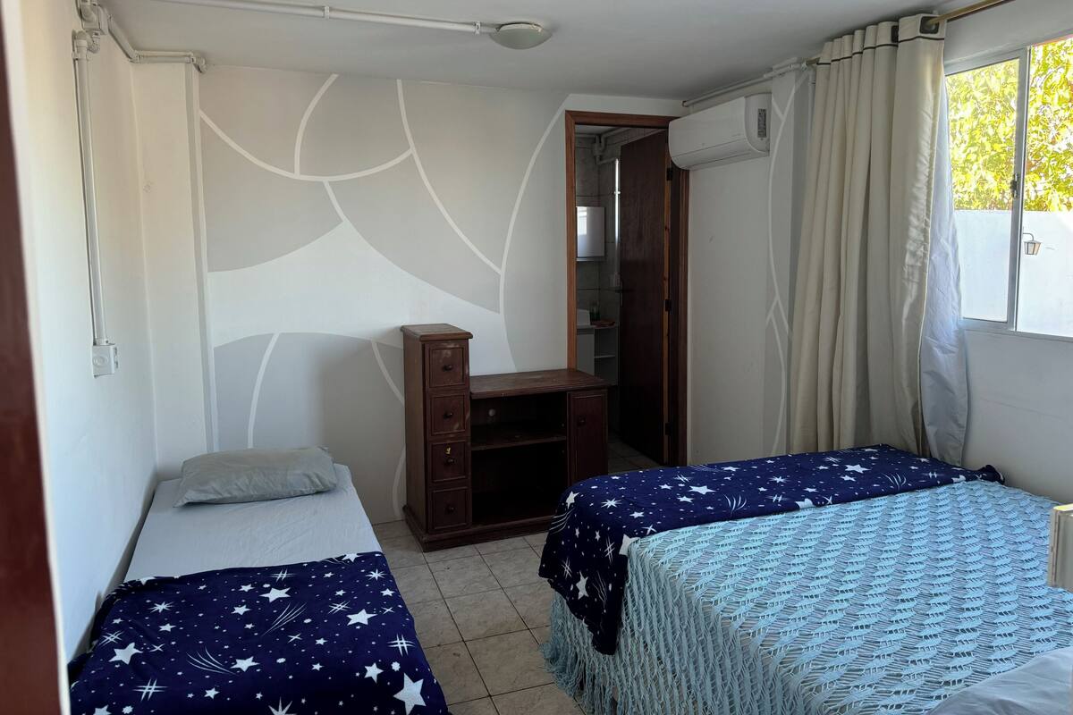 Une chambre avec deux lits, un bureau, une armoire et une fenêtre avec des rideaux.