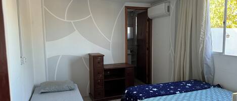 Une chambre avec deux lits, un bureau, une armoire et une fenêtre avec des rideaux.
