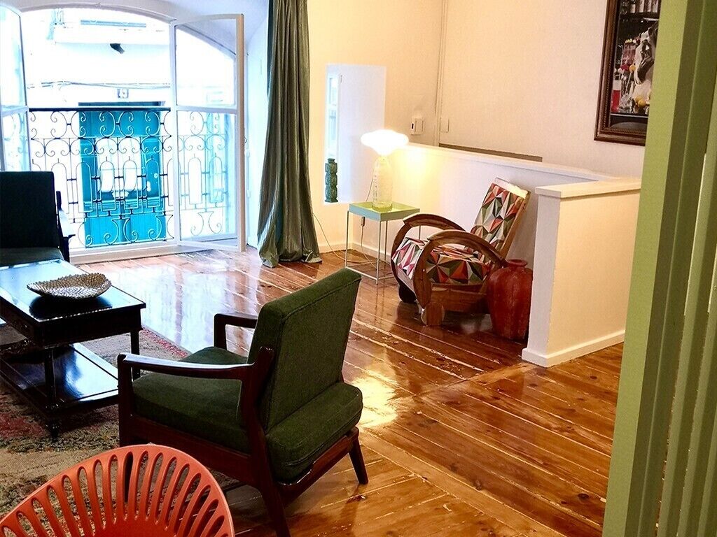 Een woonkamer met een houten vloer, een groene fauteuil, een rode stoel, een klein tafeltje met een schaal en een lamp.