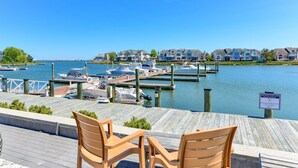 A marina with boats docked, a wooden pier with chairs, and a row of houses in the background. - Ocean Pines Hideaway (Ocean Pines)