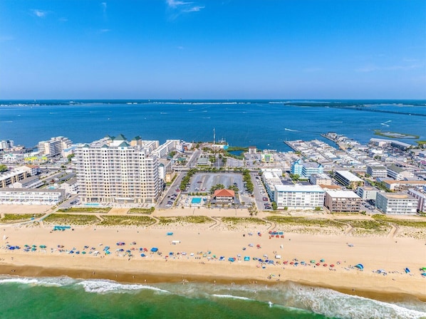 Un paisaje urbano costero con un hotel destacado, playa y puerto deportivo.