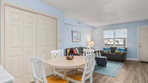 Un salon avec une table ronde, des chaises blanches, un canapé gris et un tapis bleu.