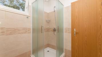 Ducha con cerramiento de vidrio, puerta de madera, paredes con azulejos color beige y ventana con vista a árboles.