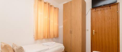 A small, single-room apartment with a bed, a wardrobe, and a television.