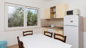 A compact kitchen with a window, a microwave, a refrigerator, and a dining table with chairs. - Holiday Home Malačnica (Supetar)