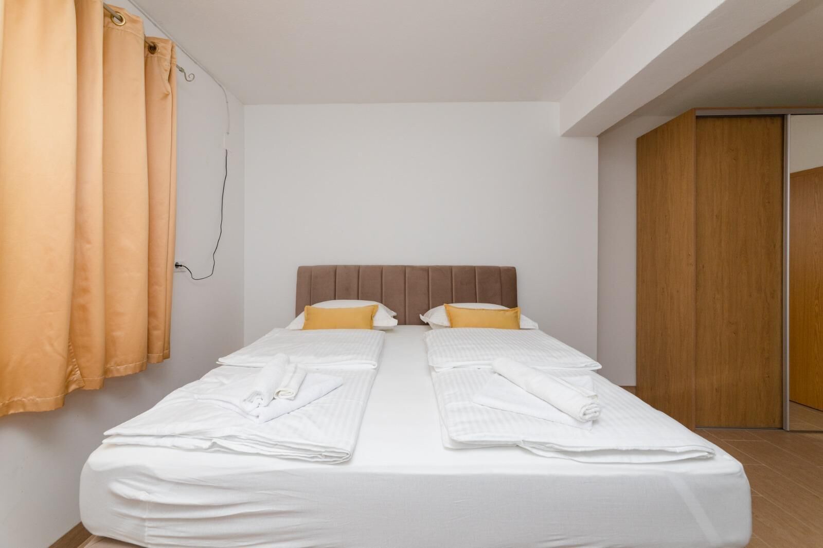A single bed with a wooden headboard, white bedding, and two yellow pillows. There are folded towels on the bed.