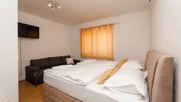 Un dormitorio con cama, sofá, televisor montado en la pared y ventana con cortinas.