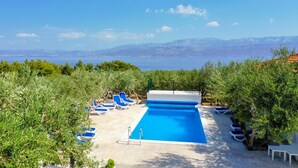 A swimming pool with blue water, surrounded by lounge chairs and trees, with a view of the sea and mountains in the background. - Holiday Home Malačnica (Supetar)