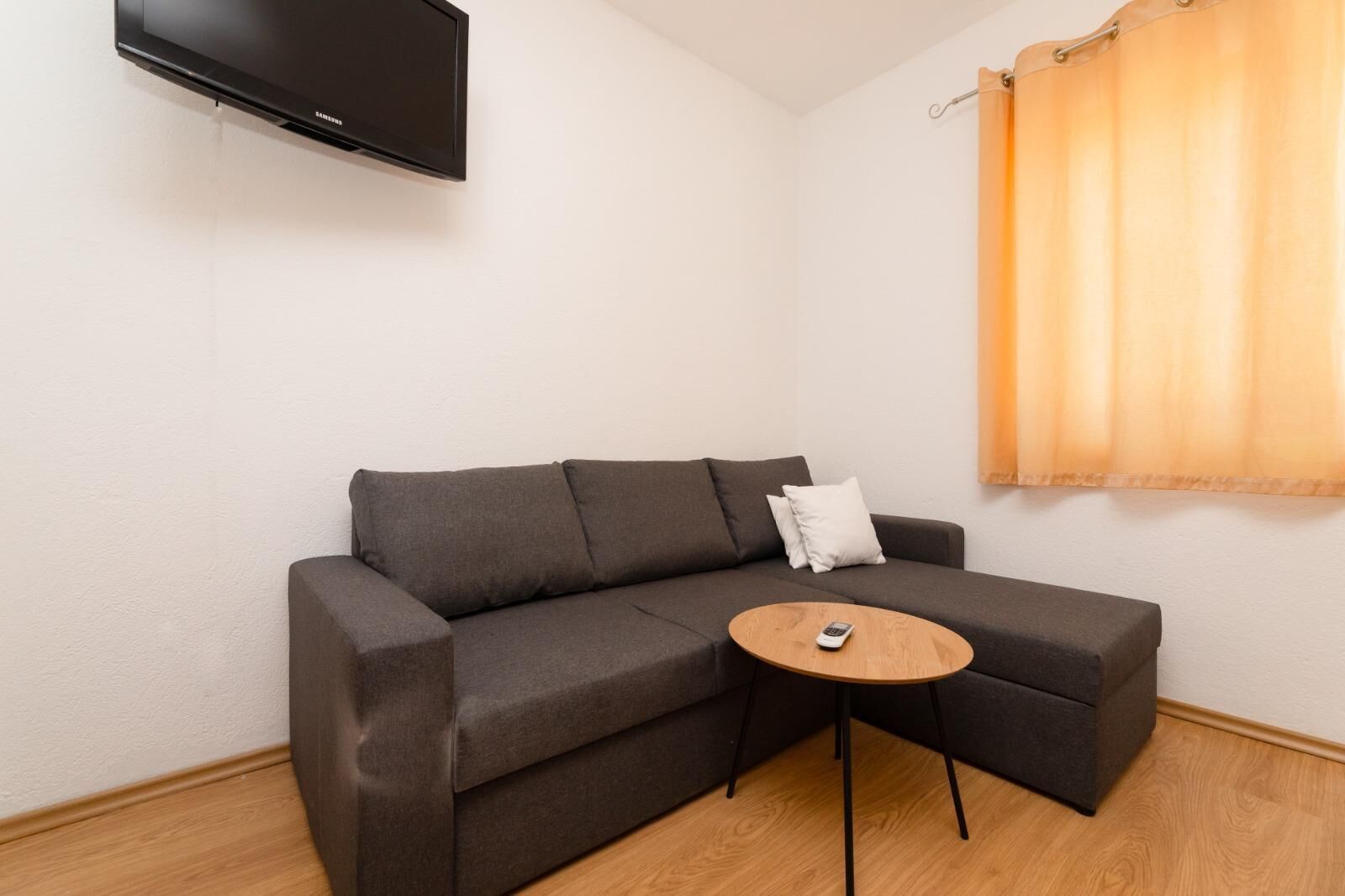 Ein modernes Wohnzimmer mit einem grauen Ecksofa, einem kleinen Holztisch und einem wandmontierten Flachbildfernseher.