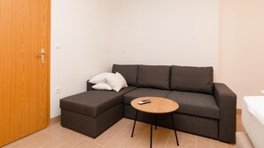 A small, modern room with a dark brown sectional sofa, a small wooden side table, and a white pillow. - Holiday Home Malačnica (Supetar)