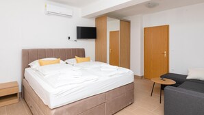 A modern hotel room with a large bed, a TV mounted on the wall, a small table, and a sofa. - Holiday Home Malačnica (Supetar)