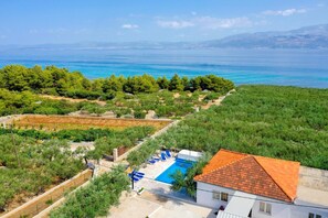 A villa with a swimming pool, surrounded by lush greenery and a view of the sea. - Holiday Home Malačnica (Supetar)