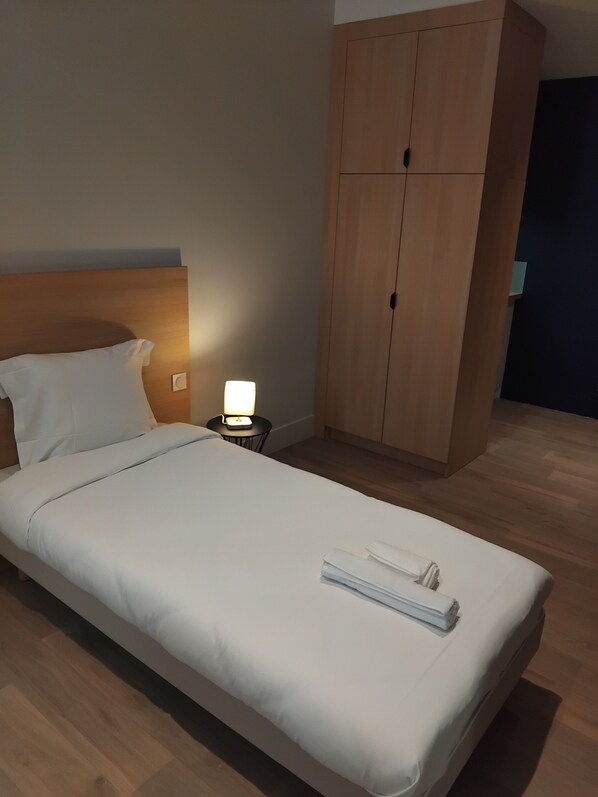 A neatly made bed with white linens, a bedside lamp, and a wooden wardrobe in a hotel room.
