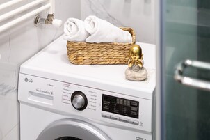 Een witte LG Direct Drive wasmachine van 6 kilogram met een bedieningspaneel, een geweven mand met handdoeken en een decoratief gouden object erop.