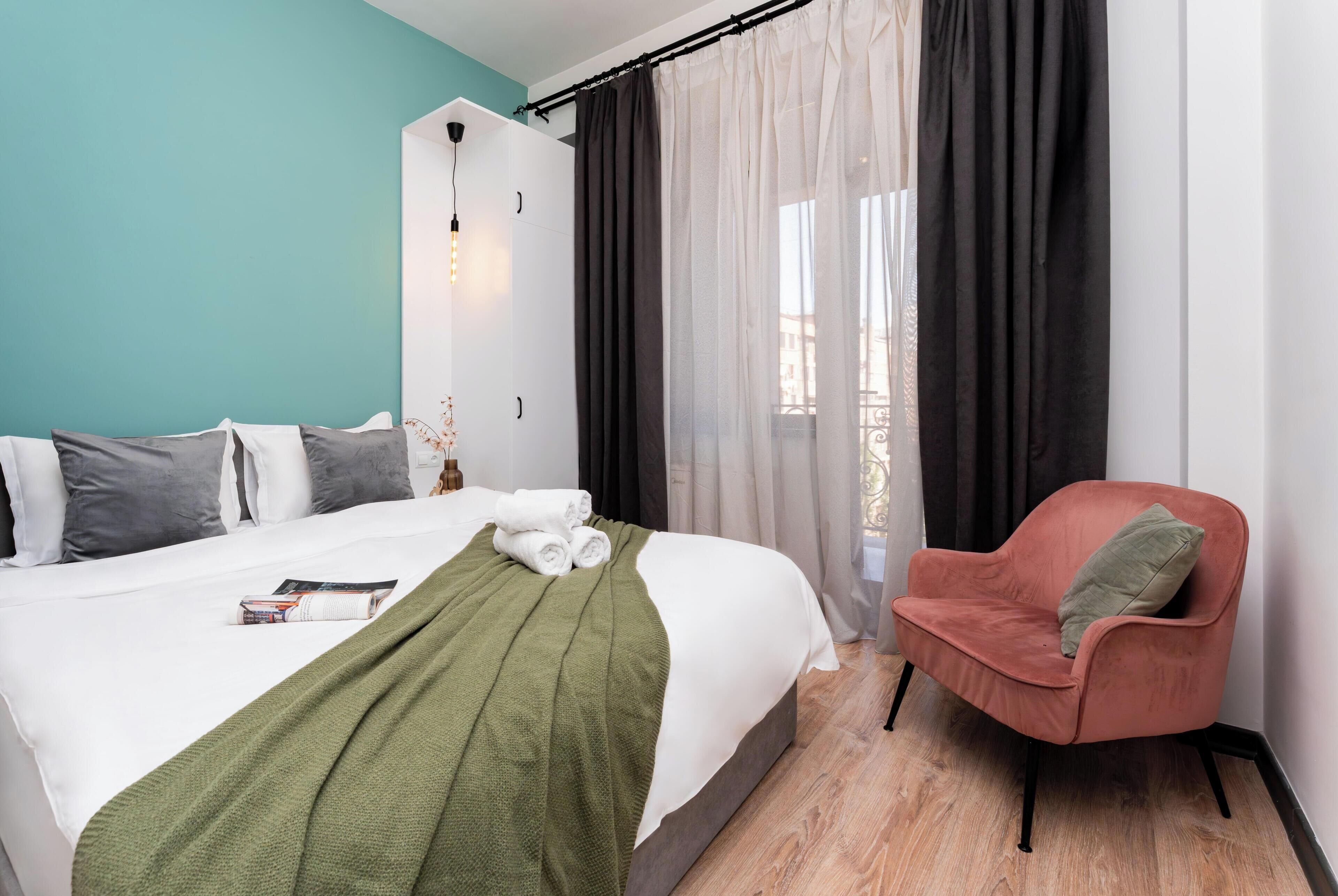 Quarto com cama, cadeira, guarda-roupa e janela com cortinas.