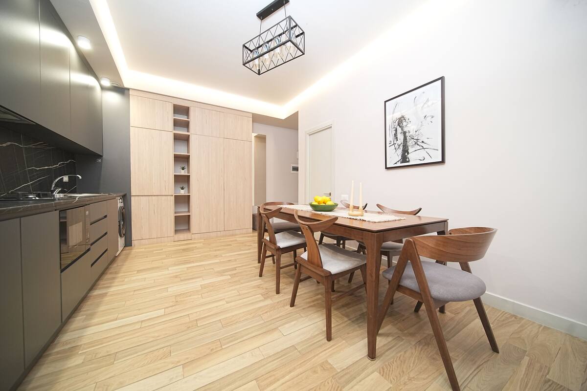 A modern kitchen with wooden cabinets, a built-in oven, and a dining area with a wooden table and chairs.