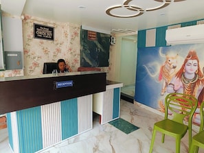 Uma mesa de recepção com a placa 'RECEPTION', uma parede coberta por papel de parede floral, um grande mural e um armário para chaves.
