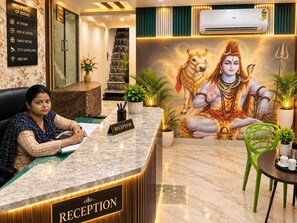 A reception desk with a sign indicating 'RECEPTION' and a list of amenities including AC rooms, non AC rooms, family rooms, CCTV surveillance, and free WiFi. - The Royal Green Residency (Varanasi)