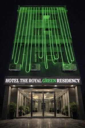 Esterno dell'Hotel The Royal Green Residency, con un'imponente insegna al neon verde e un ingresso moderno.