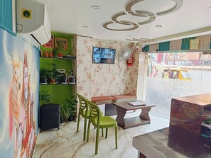 Una stanza con un murale, una televisione, una ventola, una panca e un tavolo.