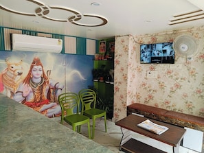 Quarto com um mural, televisão de tela plana, ventilador e um banco.