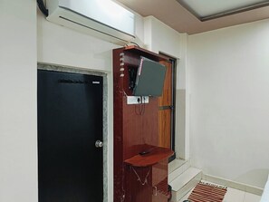 A room with a black door, a wooden shelf with a television, and a small wooden table. - The Royal Green Residency (Varanasi)