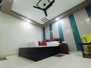 A bedroom with a bed, a ceiling fan, a nightstand, and a green chair. - The Royal Green Residency (Varanasi)