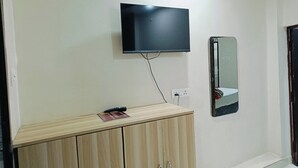 Een kamer met een aan de muur bevestigde televisie, een spiegel en een houten kastje met een afstandsbediening erboven.