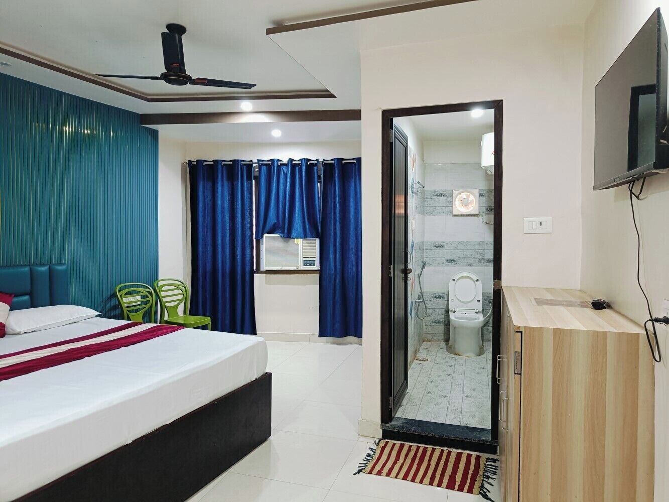 A hotel room with a bed, a TV, a shower, and a bathroom with a toilet.